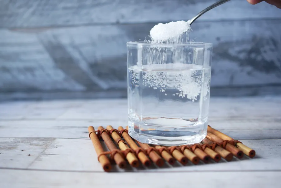 Magnesium Glycinate vs Citrate: Which One Should You Buy? 3 A spoonful of white powder held above a glass of water on a bamboo mat